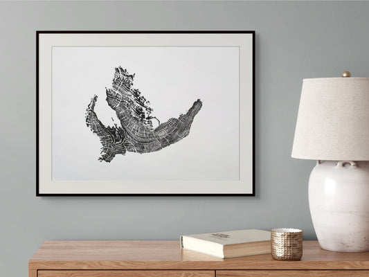 Black framed print of a tree root monoprint with concentric rings, hanging above a wooden side table.