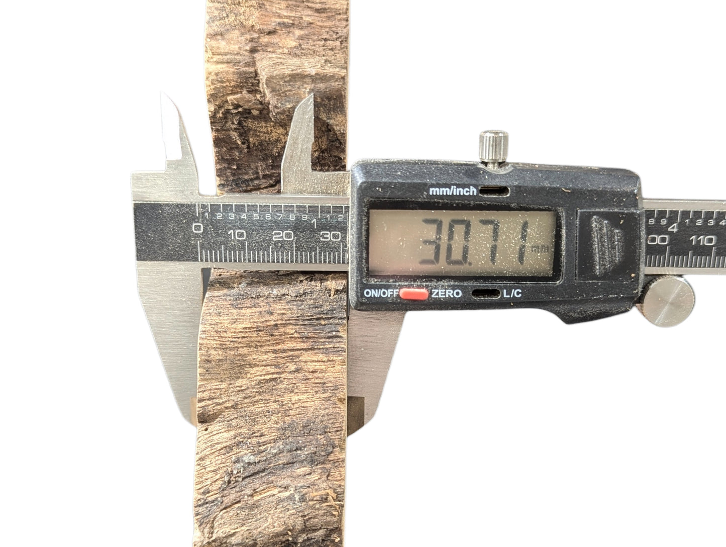 Digital caliper measuring a textured, light brown wood piece, displaying a 30.71mm thickness measurement.