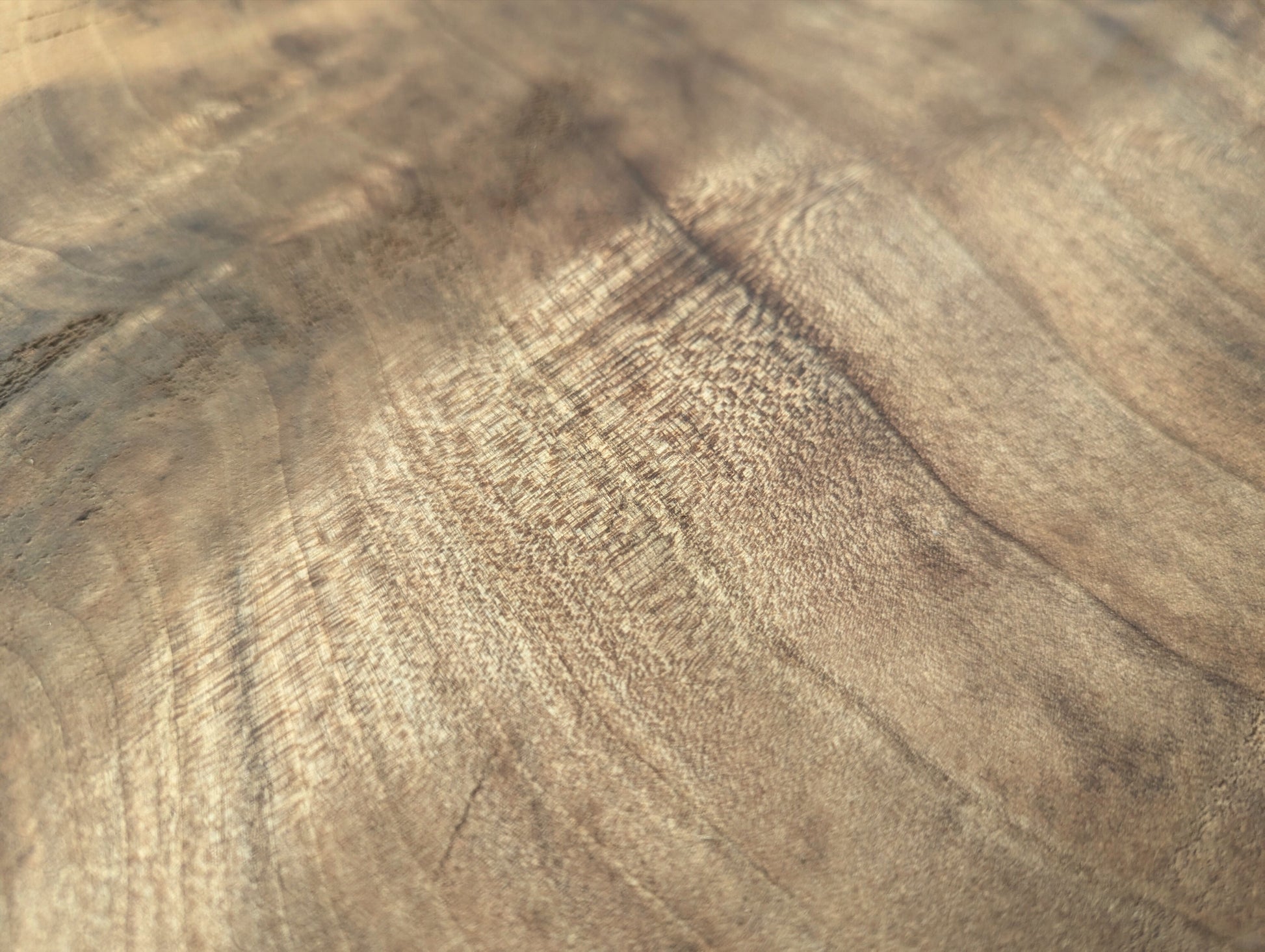 Close-up of a light brown wood surface, showcasing prominent swirling grain patterns and a figured, rippled texture.