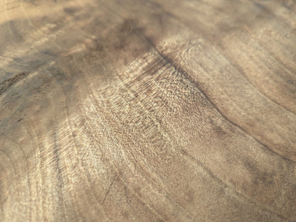 Close-up of a light brown wood surface, showcasing prominent swirling grain patterns and a figured, rippled texture.