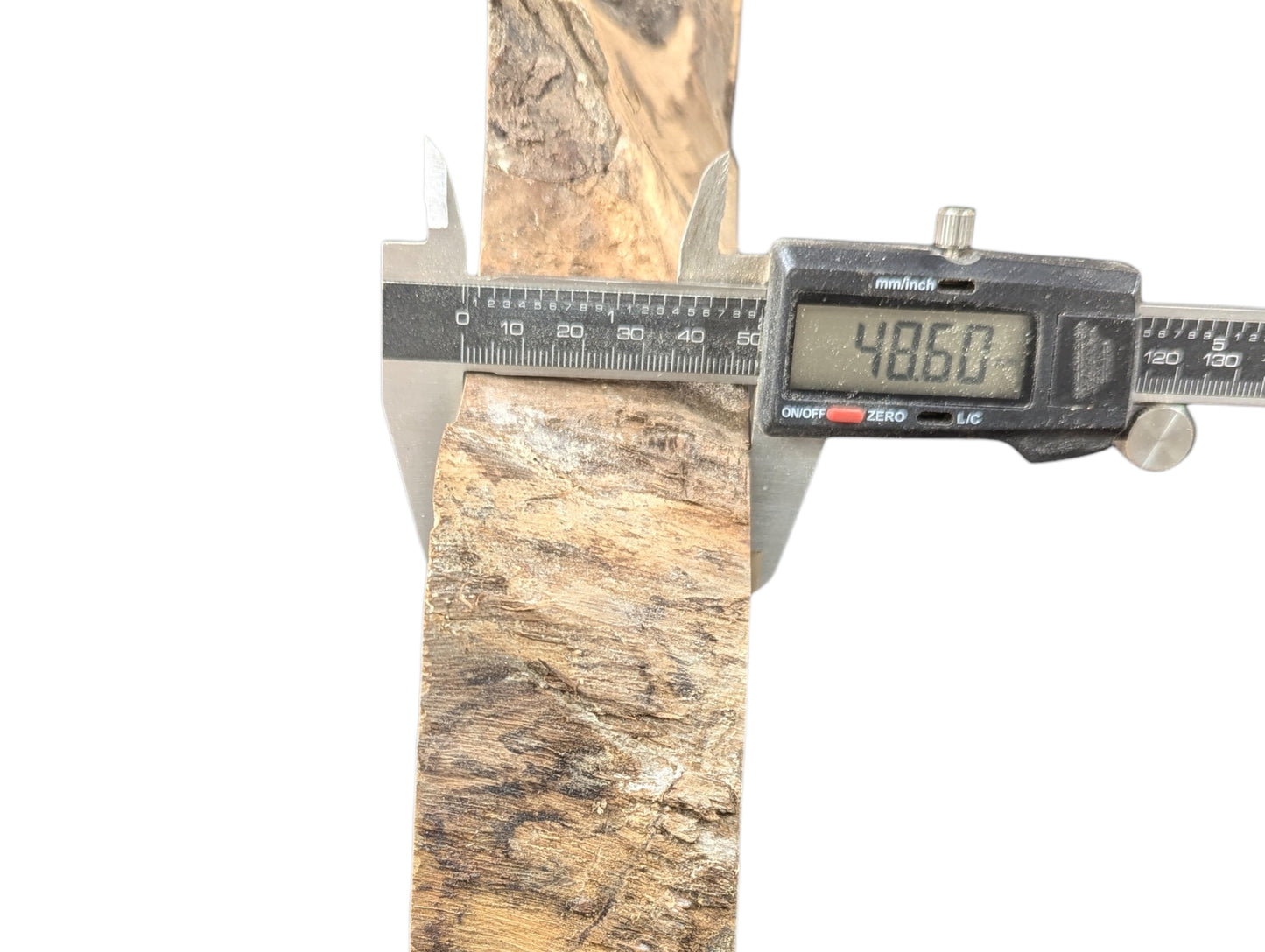 Digital caliper measuring a light and dark brown wood slice with textured surfaces, showing 48.60 mm.
