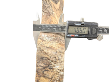 Digital caliper measuring a light and dark brown wood slice with textured surfaces, showing 48.60 mm.