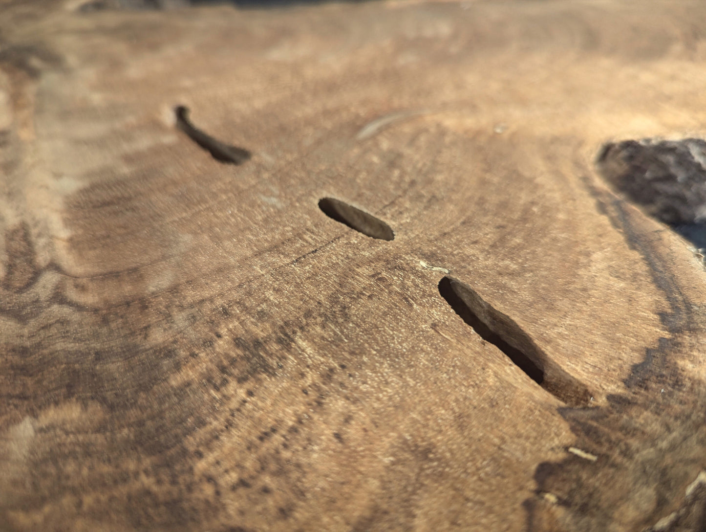 Surface of a light brown wood slice showing three dark, elongated fissures and swirling grain patterns.