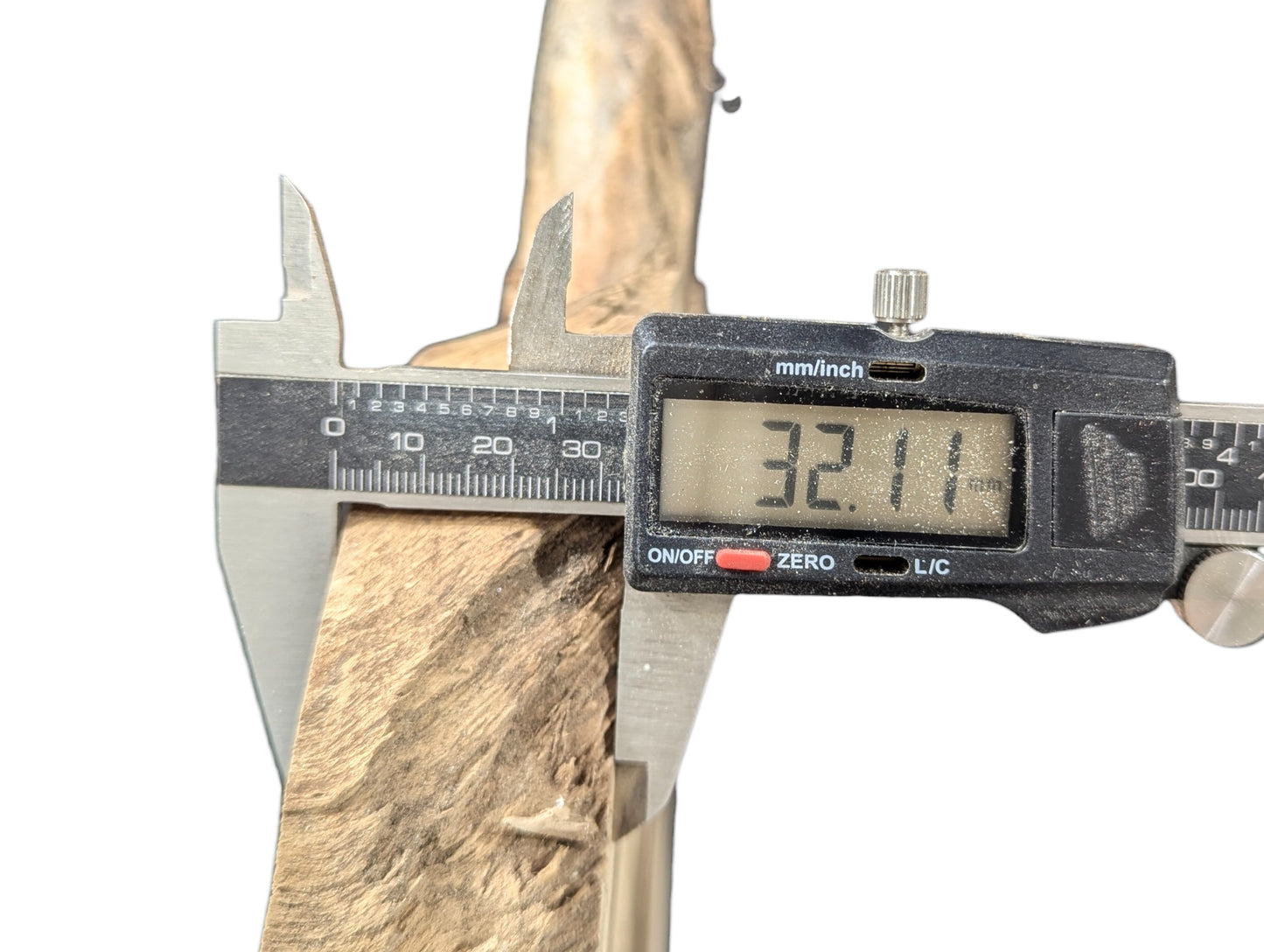 Digital caliper measures the 32.11 mm thickness of a light brown, rough-textured wood slice.
