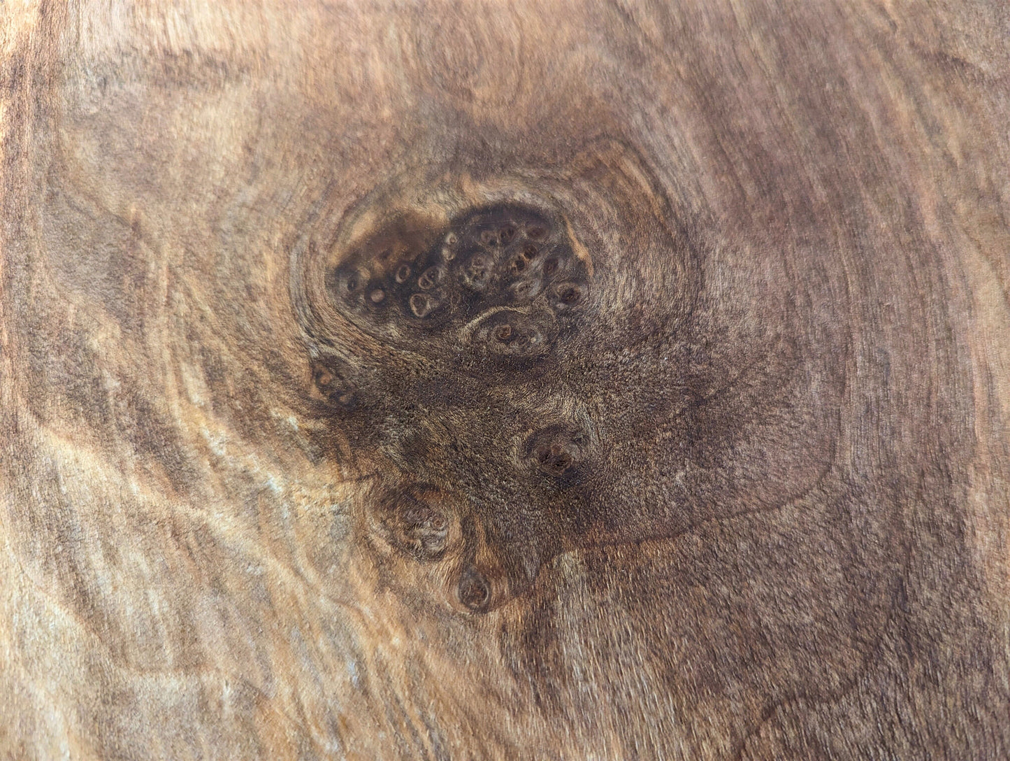 Varied brown wood grain close-up, highlighting a dark central knot with several smaller, darker eye-like features.