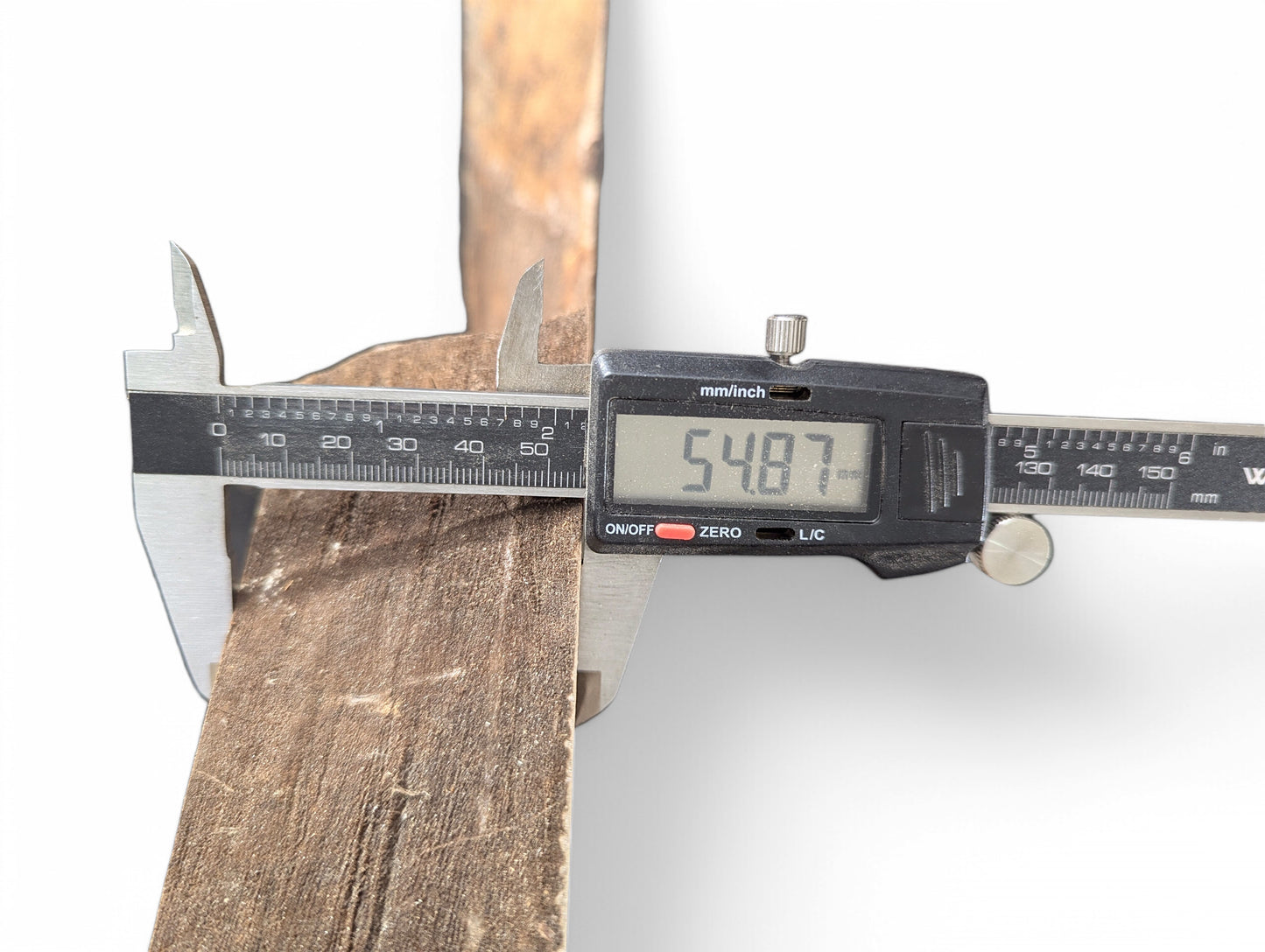 A digital caliper measures the rough, brown side of a wood slice, displaying 54.87mm.
