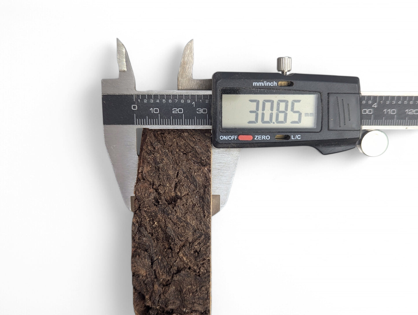 A digital caliper measures the dark brown, textured side of a wood piece, displaying 30.85 mm.