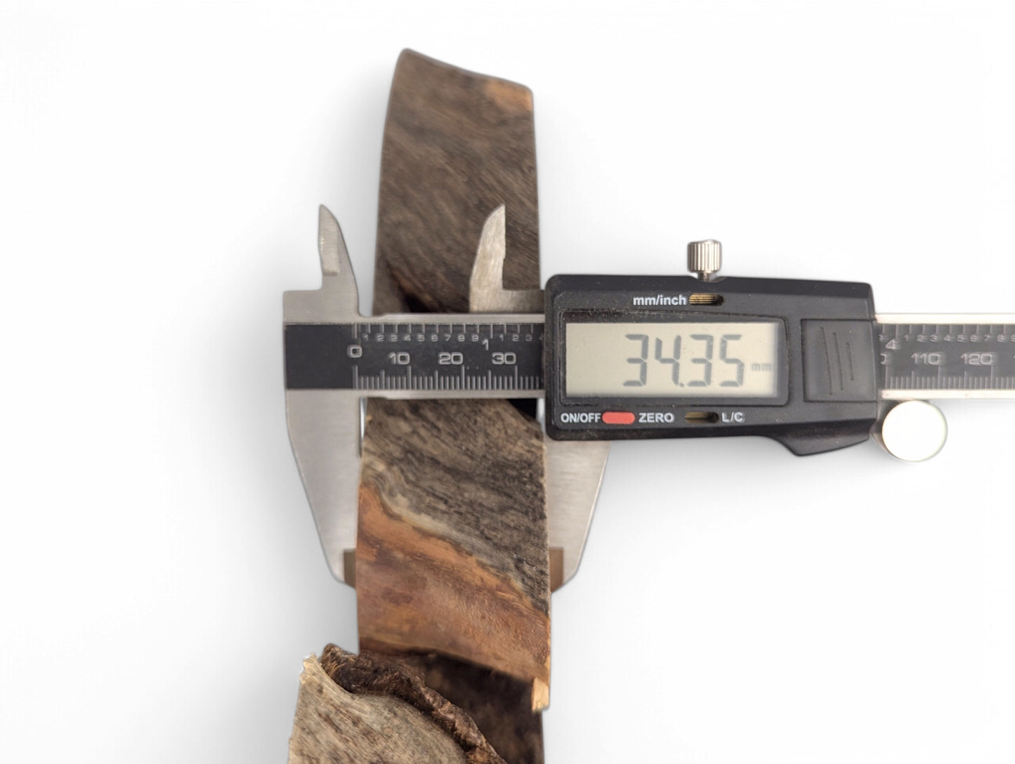 Digital caliper measures a dark brown and reddish-brown wood slice, displaying a thickness of 34.35 mm.