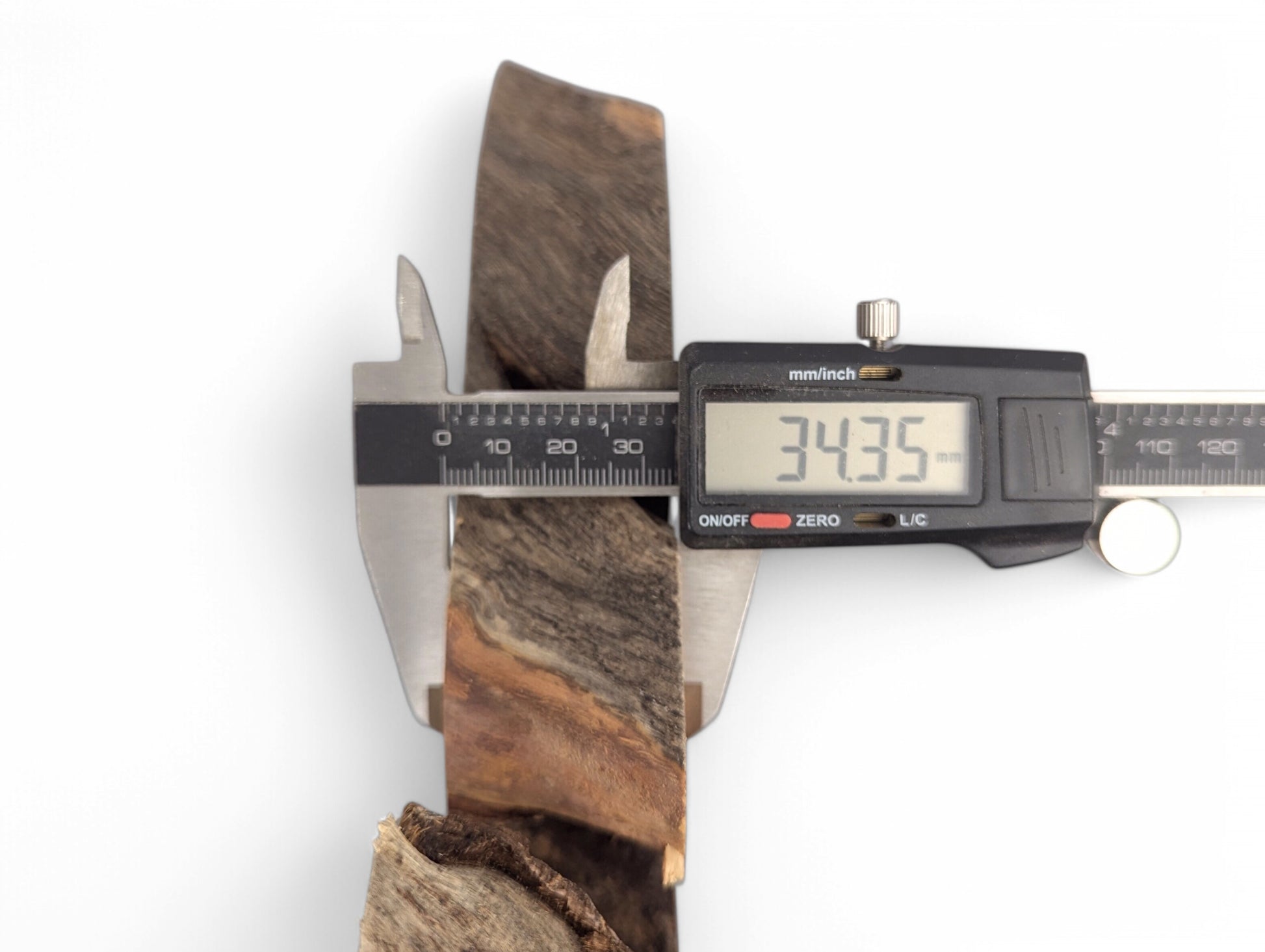 Digital caliper measures a dark brown and reddish-brown wood slice, displaying a thickness of 34.35 mm.