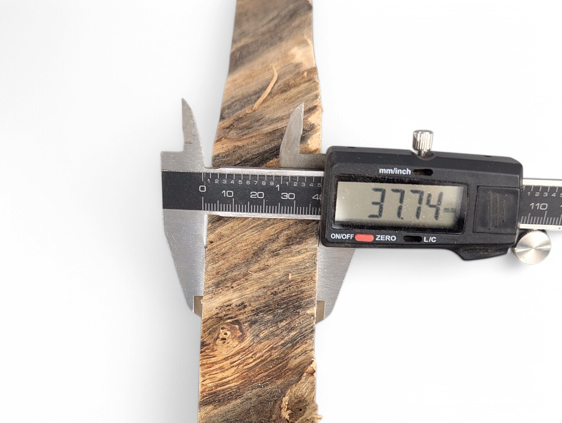 Digital caliper measures a textured, irregular brown wood slice, displaying 37.74 mm on its screen.