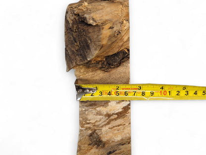 Textured light brown wood piece with rough edges and dark markings, measured by a yellow tape.