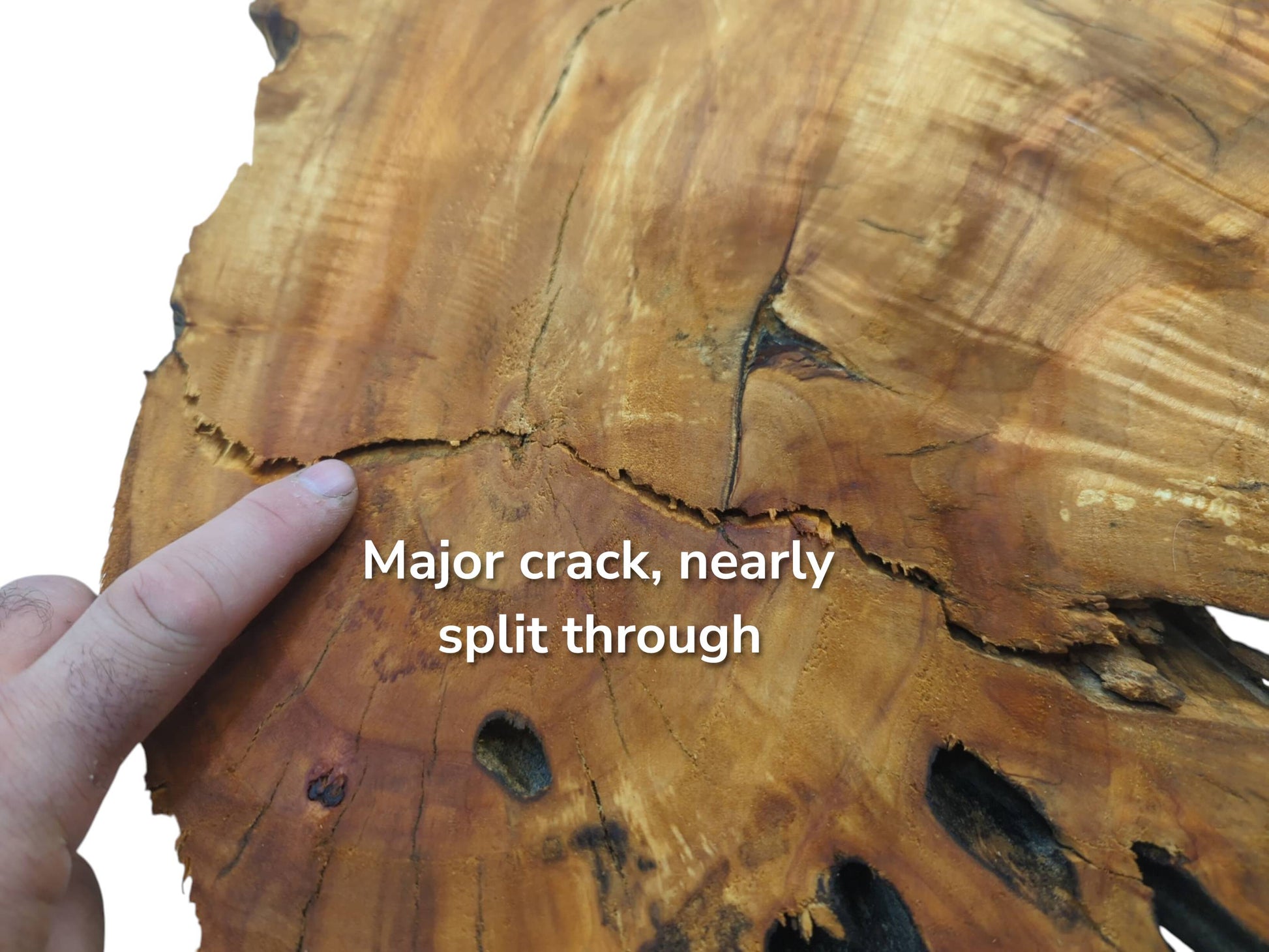 A finger points to a major crack nearly splitting through a light brown wood slab.