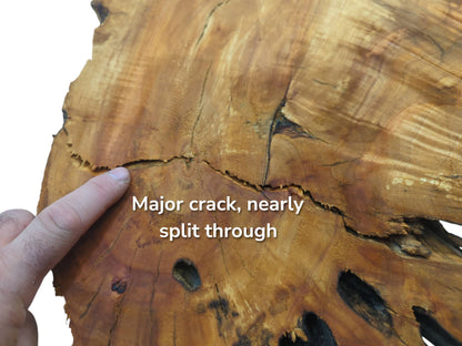 A finger points to a major crack nearly splitting through a light brown wood slab.