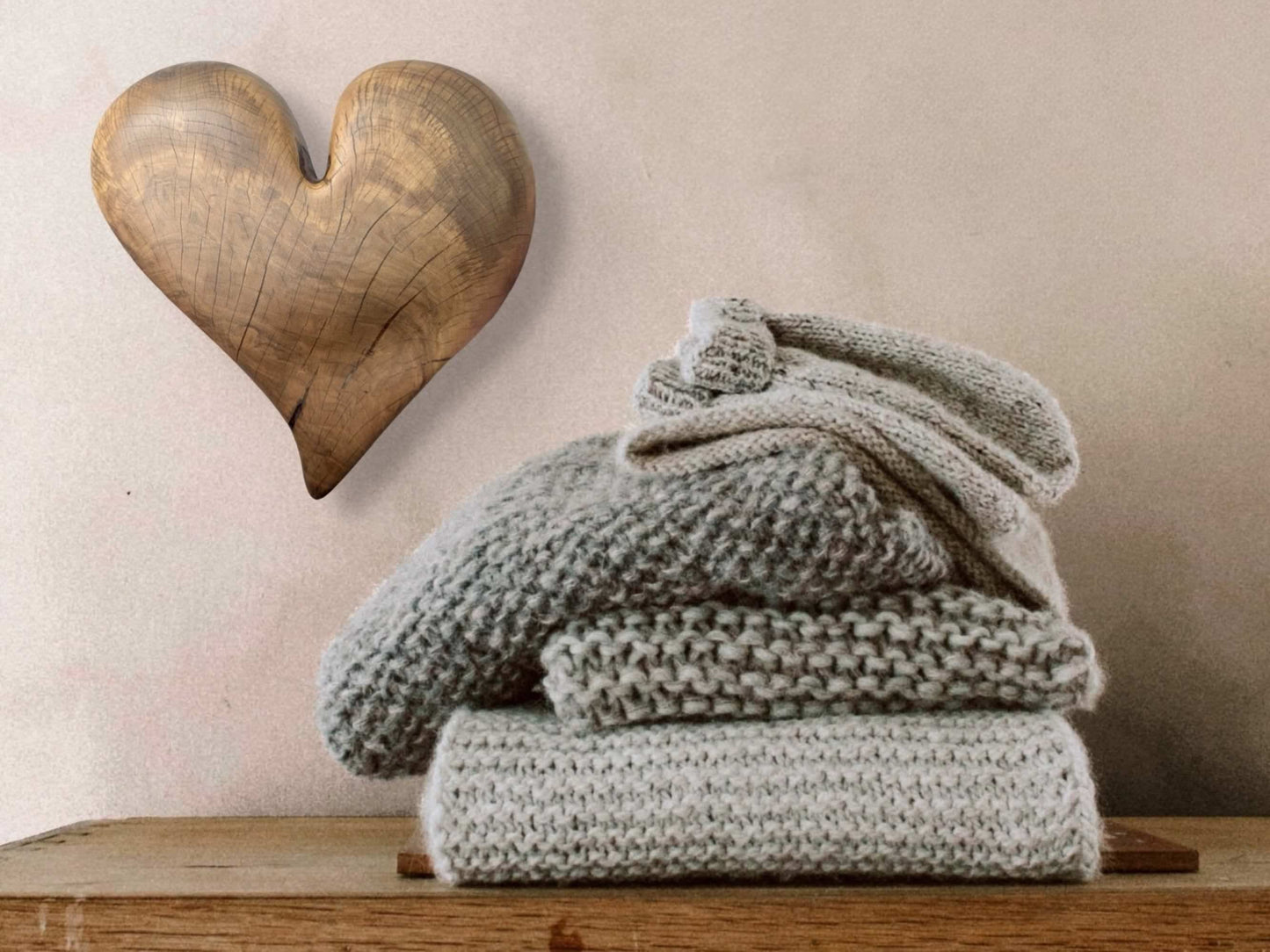 A hand-carved wooden heart, displaying natural grain and cracks, hangs above stacked gray knitwear.