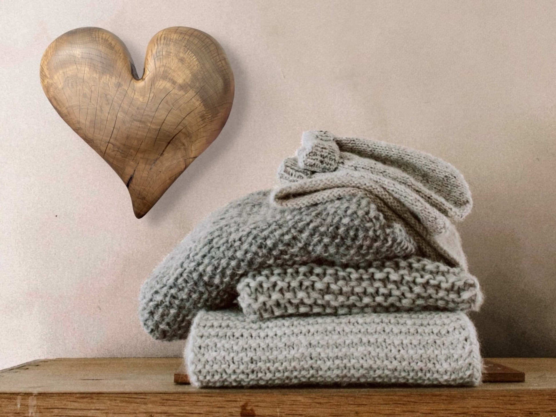 A hand-carved wooden heart, displaying natural grain and cracks, hangs above stacked gray knitwear.