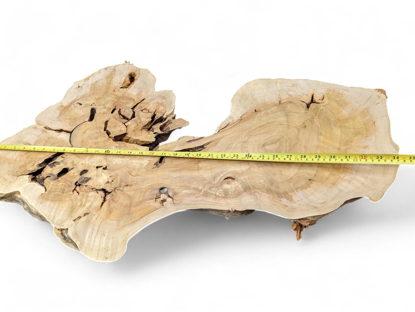 Light-colored, irregular wood slice with natural edges, voids, wavy grain, and a yellow measuring tape.