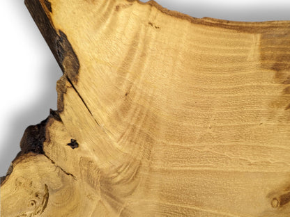 Irregular light brown live edge wood slice showing wavy grain, dark bark, and a diagonal crack.