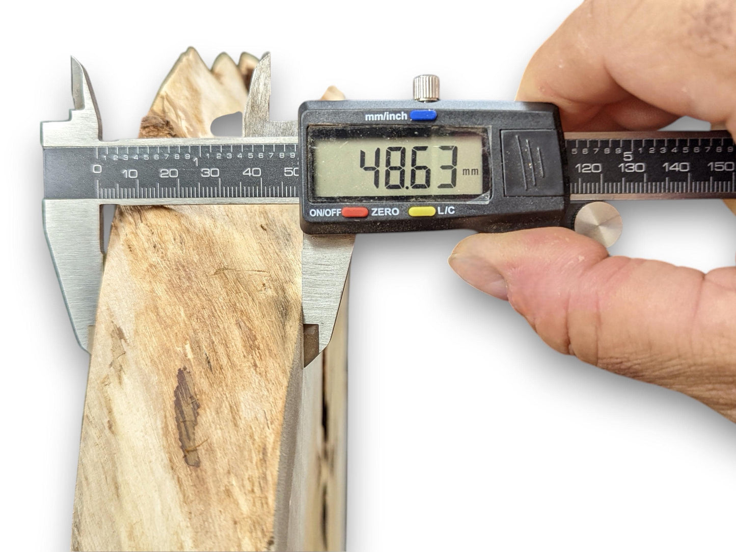 A digital caliper held by a hand measures the thickness of a light brown wood slab to 48.63mm.