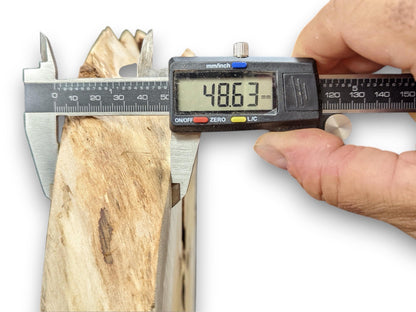 A digital caliper held by a hand measures the thickness of a light brown wood slab to 48.63mm.