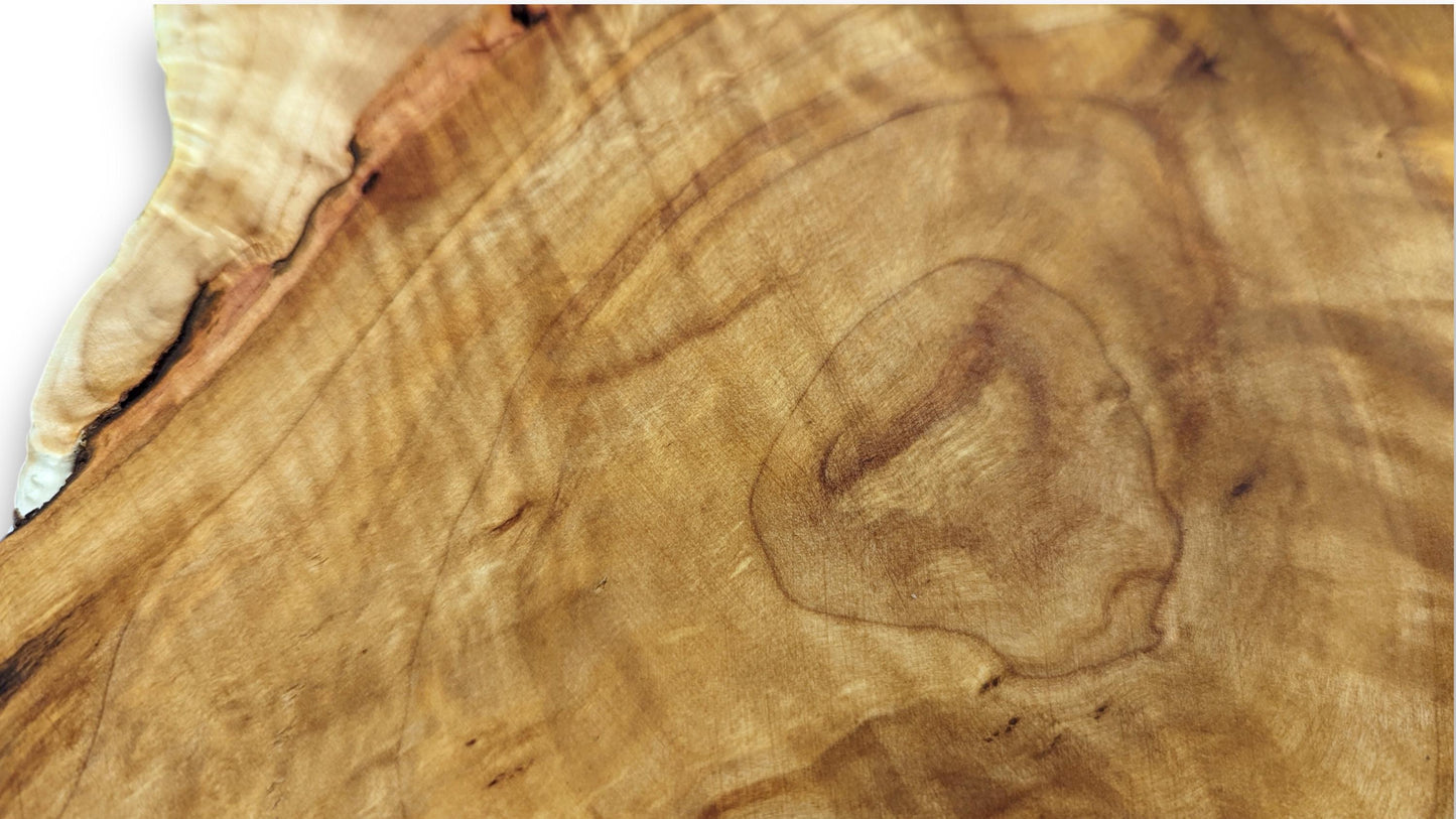 Golden-brown wood surface featuring intricate wavy grain patterns, darker lines, and a light, irregular live edge.