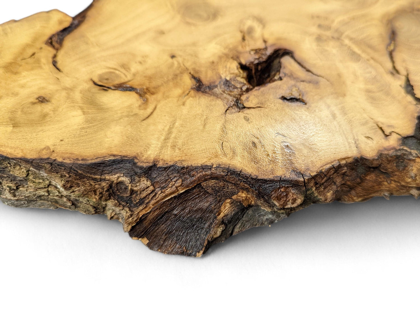 Close-up photo of an irregular, light brown wood slice showing live edge bark and prominent grain patterns.