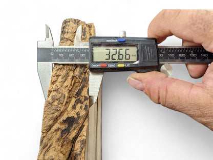 A hand holds a digital caliper measuring a textured brown wood piece to 32.66 mm.