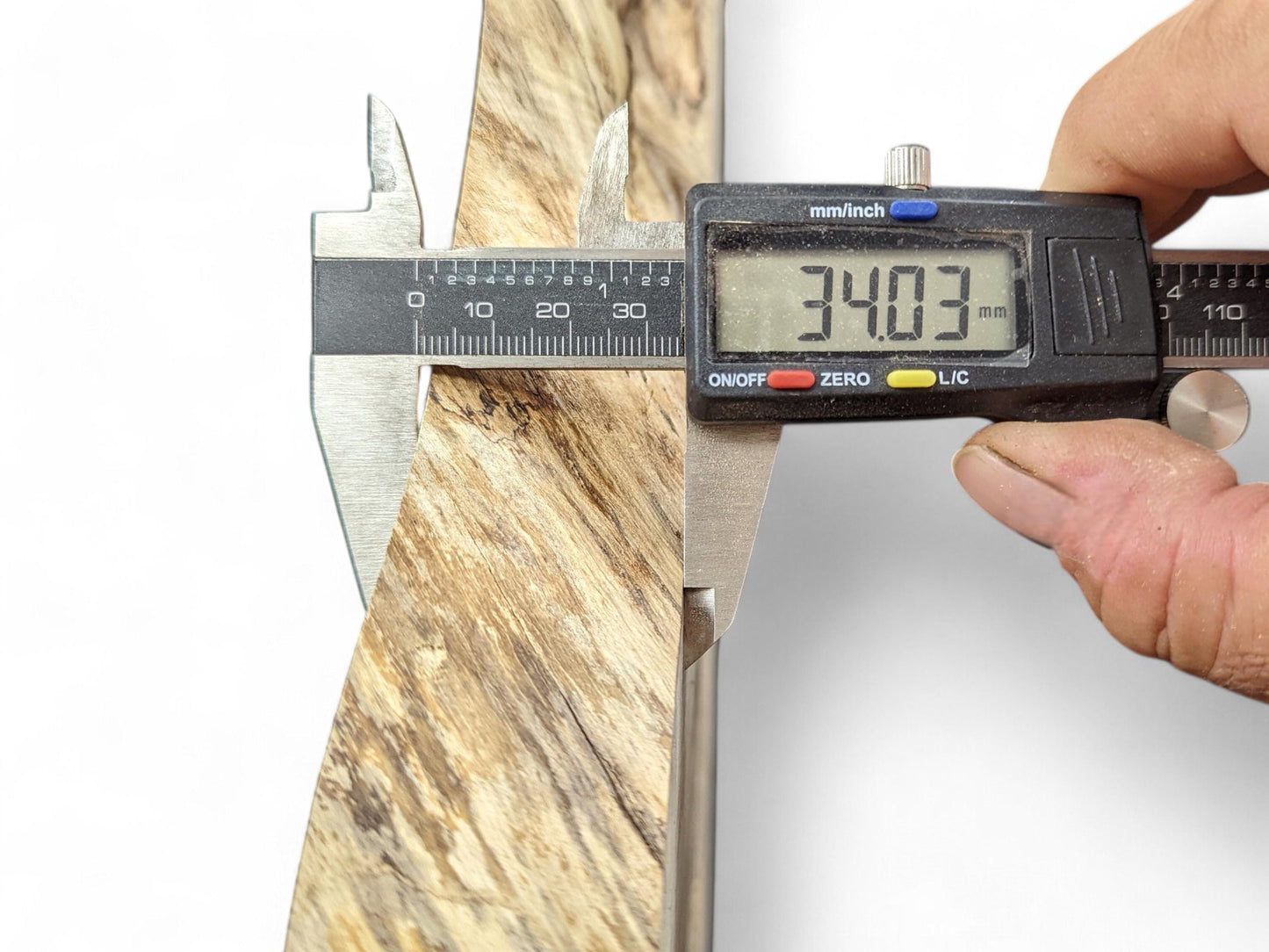 Close-up of a digital caliper measuring a light brown wood root slice, displaying 34.03 mm.