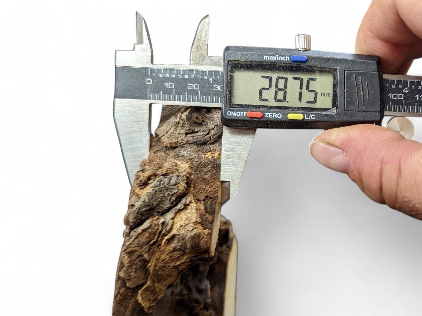 Digital caliper measuring the thickness of a dark brown, rough piece of wood to 28.75 mm.