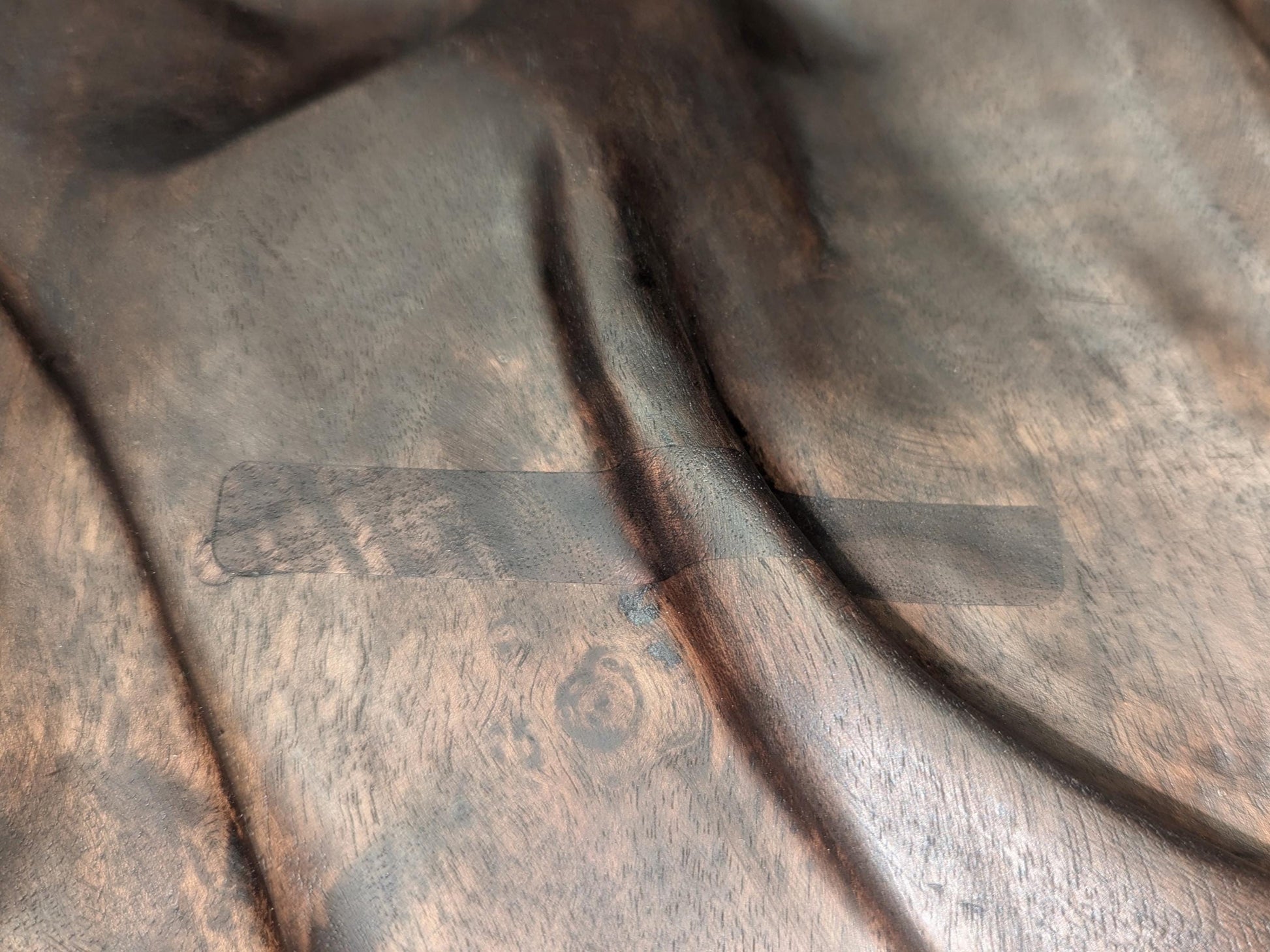 Close-up of dark brown carved walnut, fabric-like relief, showing a rectangular repaired surface patch.