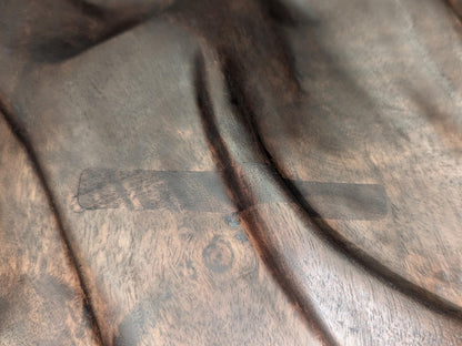 Close-up of dark brown carved walnut, fabric-like relief, showing a rectangular repaired surface patch.