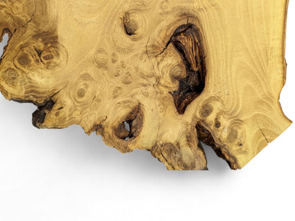 Golden-brown wood slice featuring intricate swirling grain, multiple burls, a dark void, and irregular live edge.