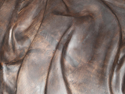 Textured dark brown walnut wood carving showing undulating folds and two rectangular repairs.
