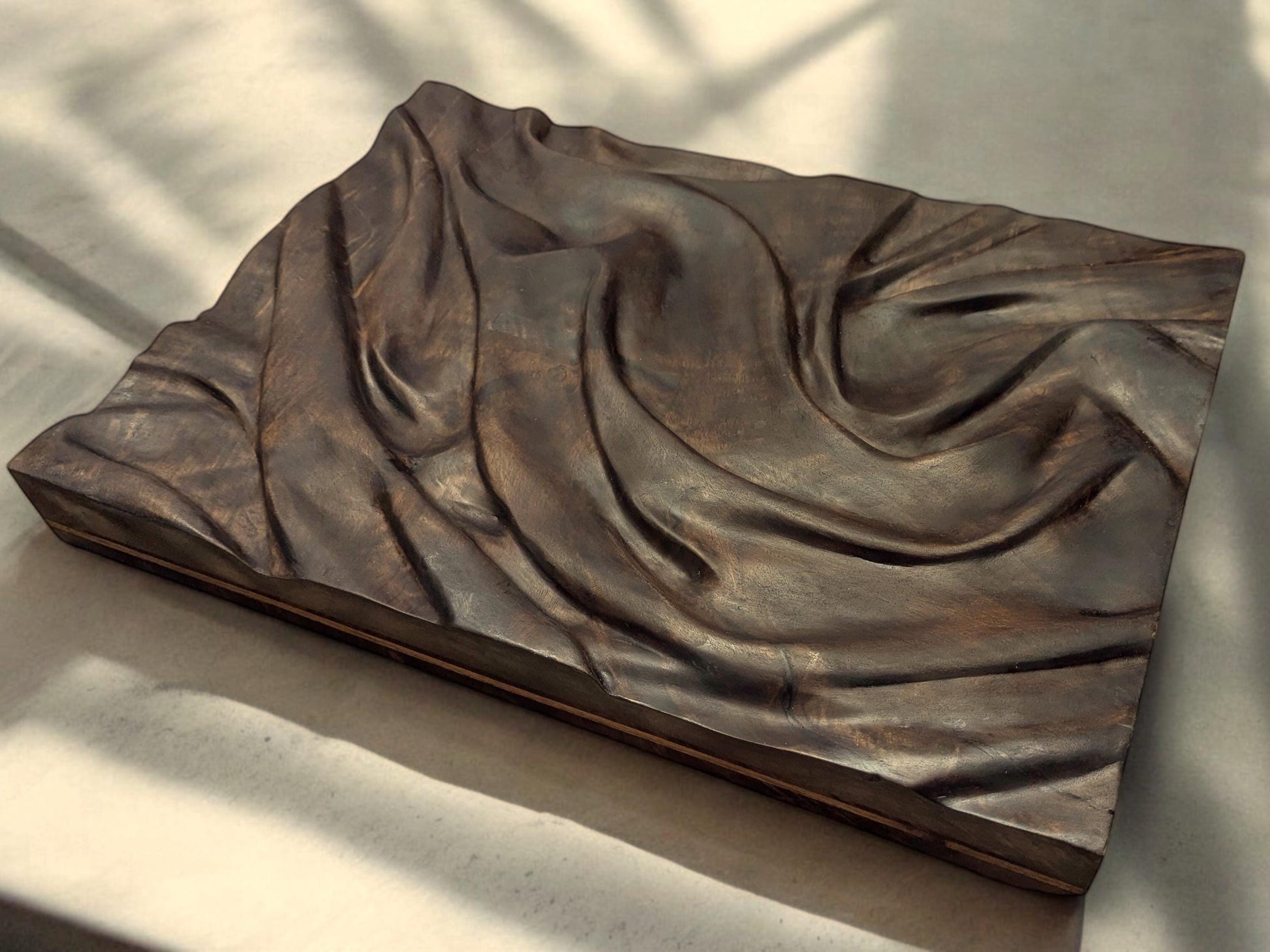 Dark brown carved walnut wall art showing a fabric-inspired relief, treated with natural oils.