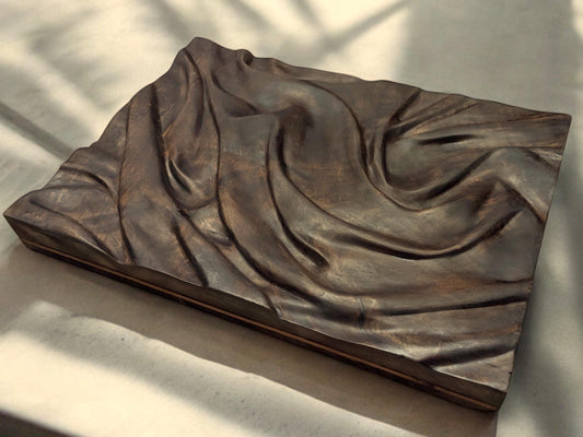 Dark brown carved walnut wall art showing a fabric-inspired relief, treated with natural oils.