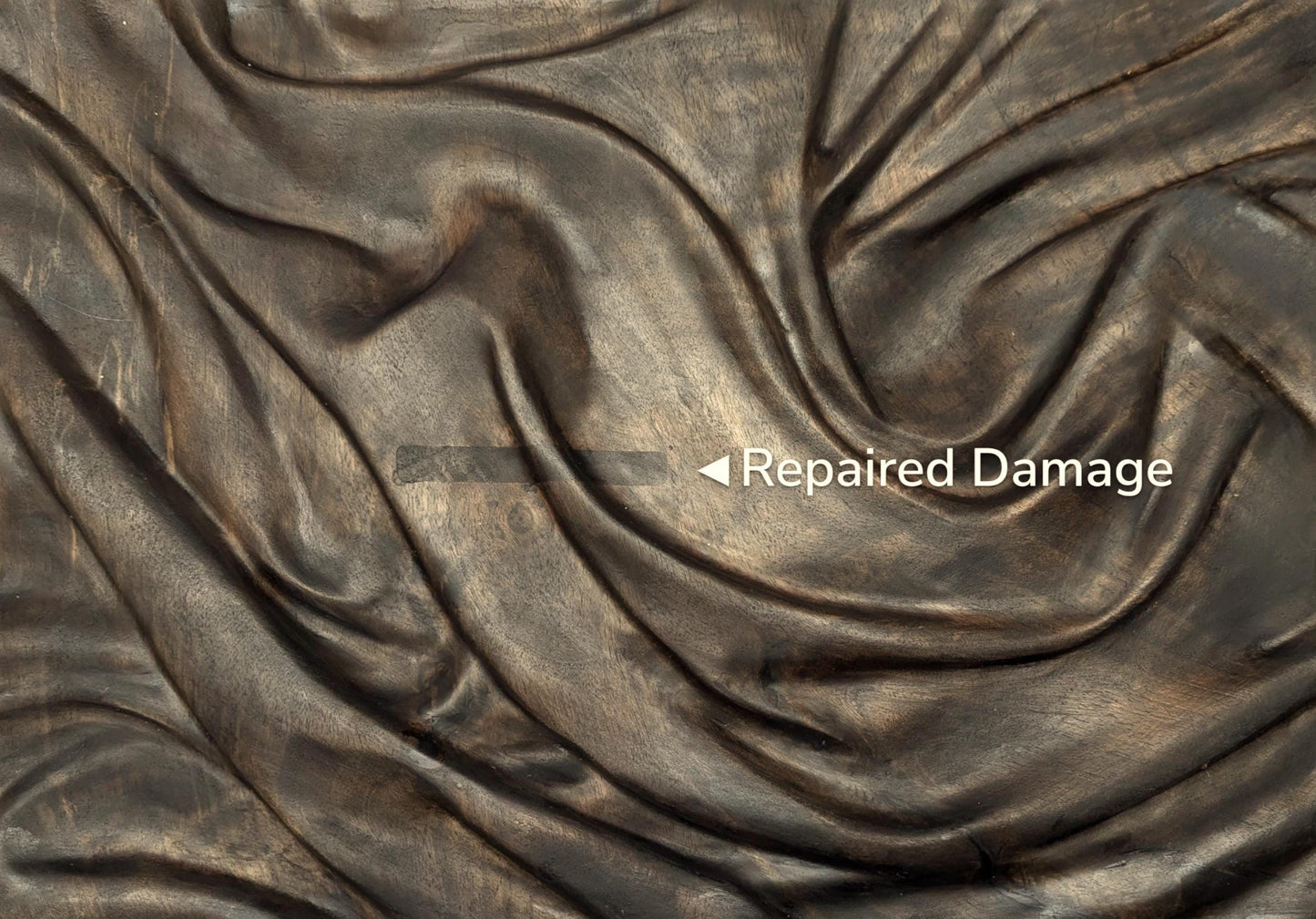 A close-up of dark, carved wood with a text overlay indicating a repaired area.