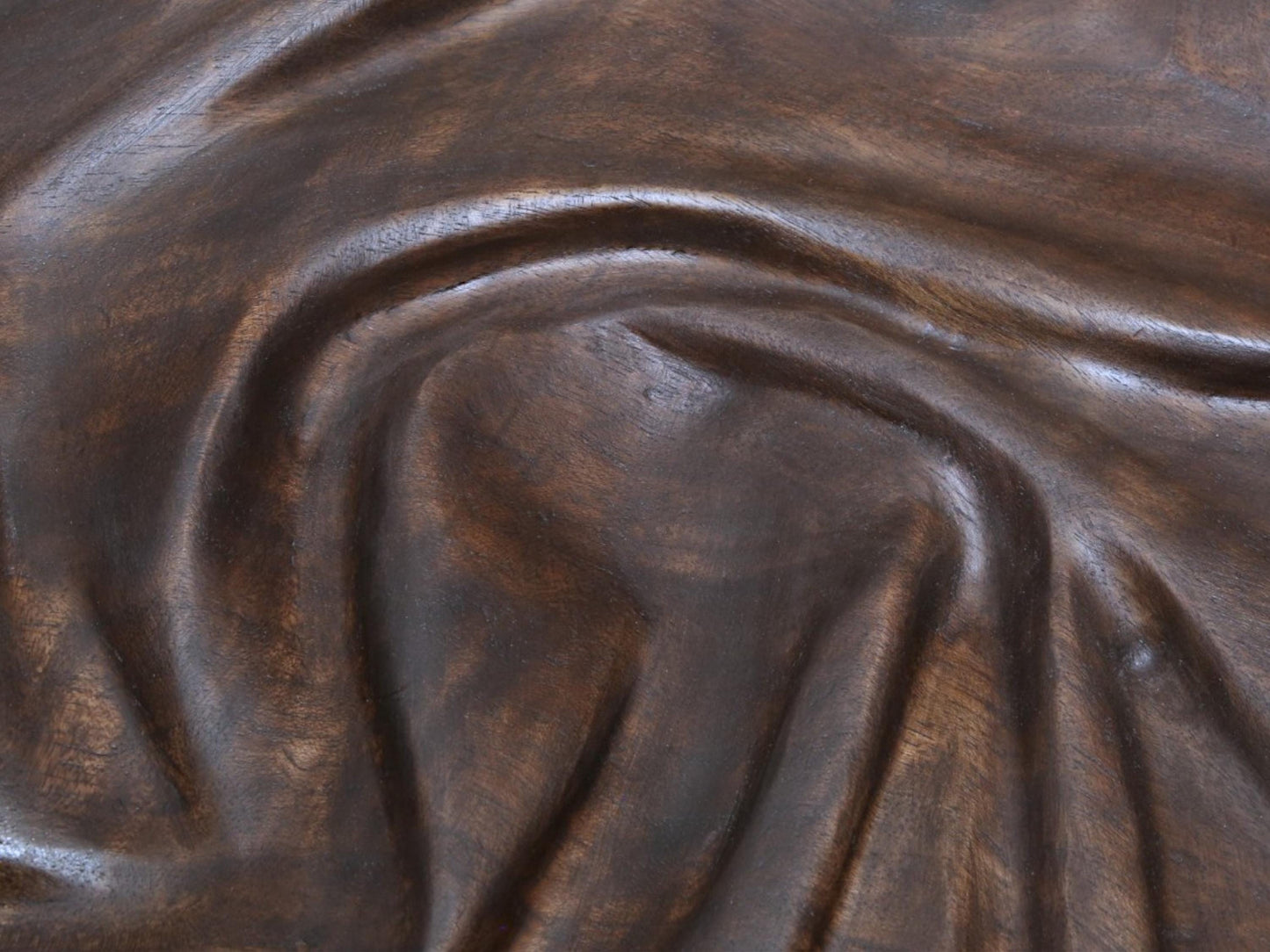 Wood carving of dark brown walnut features deep, flowing fabric-like folds, treated with natural oils.