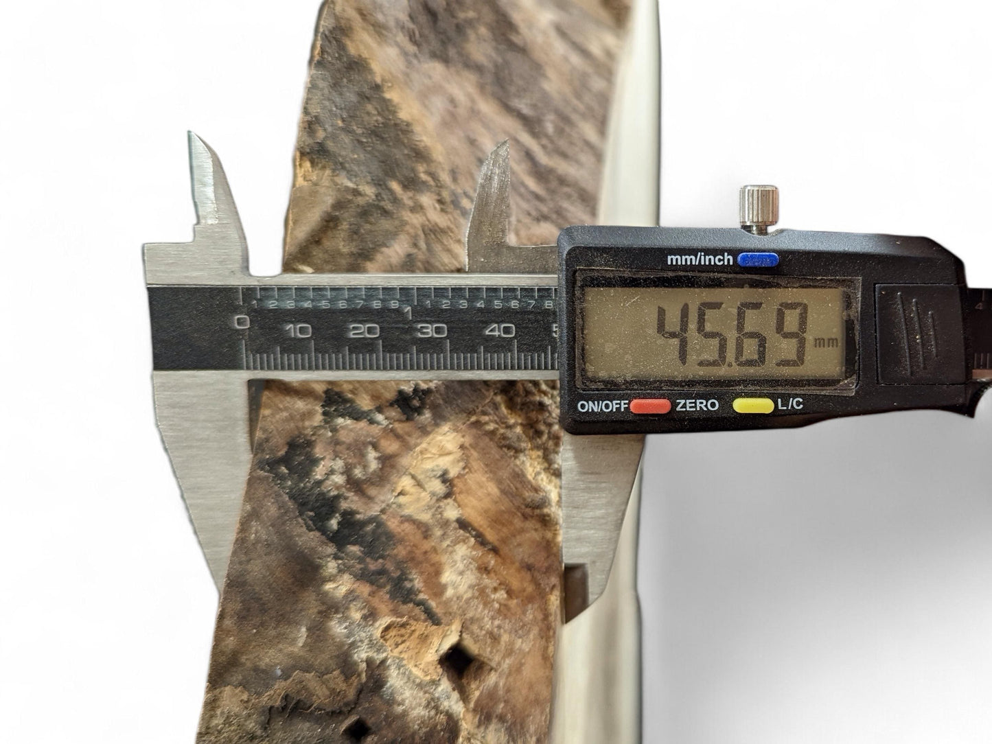 Digital caliper displays 45.69 mm, measuring the thickness of a dark and light brown live edge wood slice.