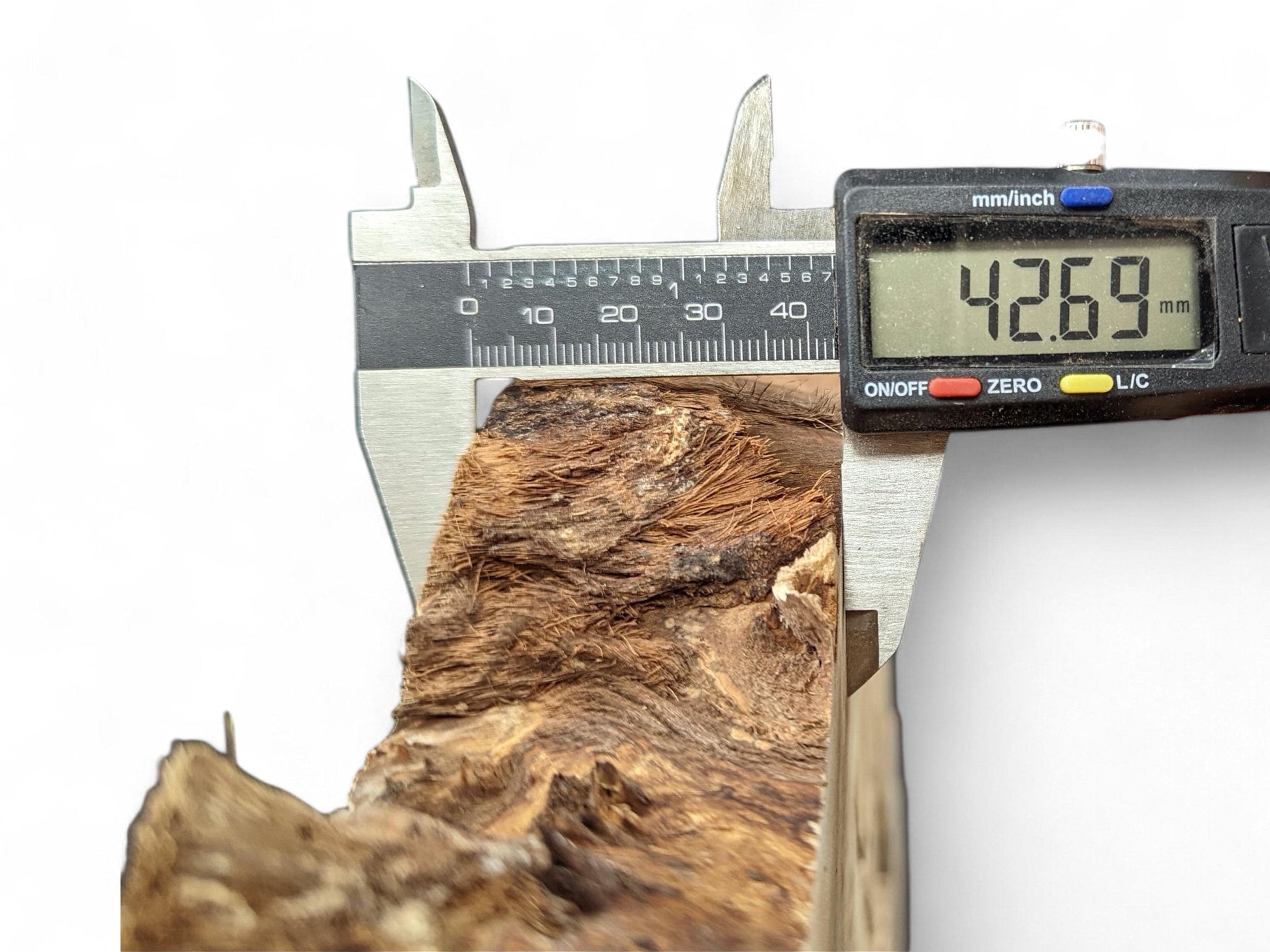 Digital caliper measuring a textured, reddish-brown wood piece with fibrous detail, displaying 42.69 mm.