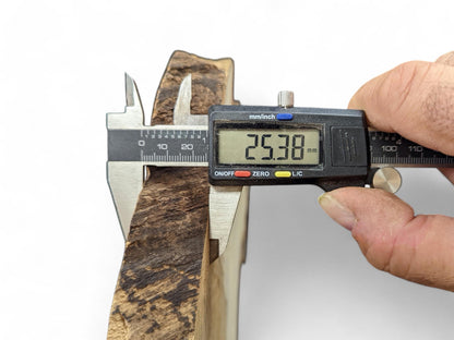Digital caliper measures a dark brown, irregularly textured wood slice, displaying 25.38 mm thickness.