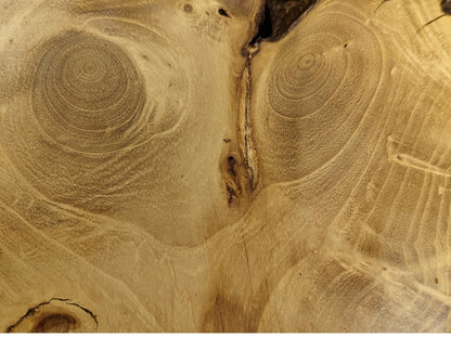 Grains of a light brown wood slice, featuring two prominent swirling knots and a dark vertical crack.