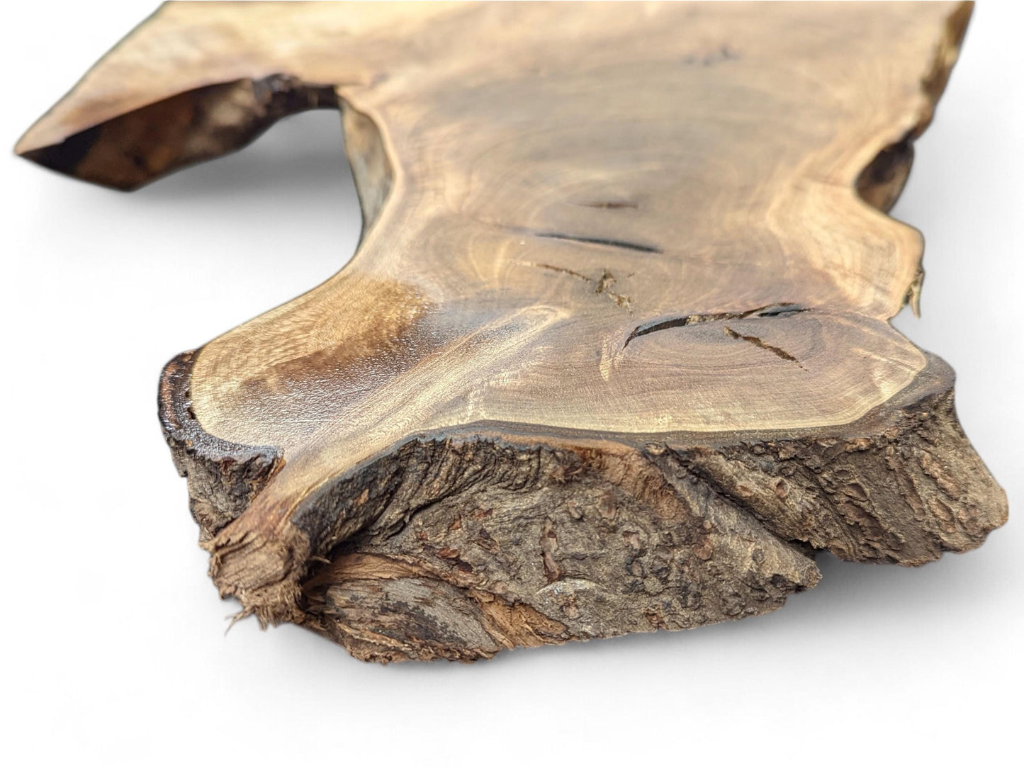 Irregularly shaped light brown live edge wood slice displaying swirling grain patterns, cracks, and textured bark.
