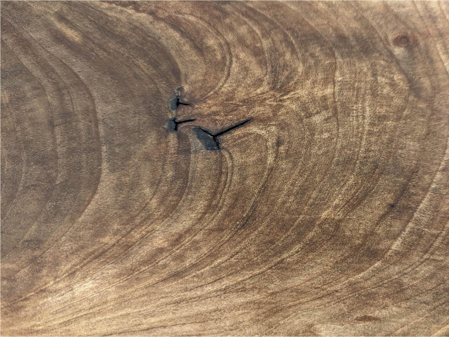 Brown wood surface showing intricate swirling grain patterns, a dark central knot, and several radiating splits.