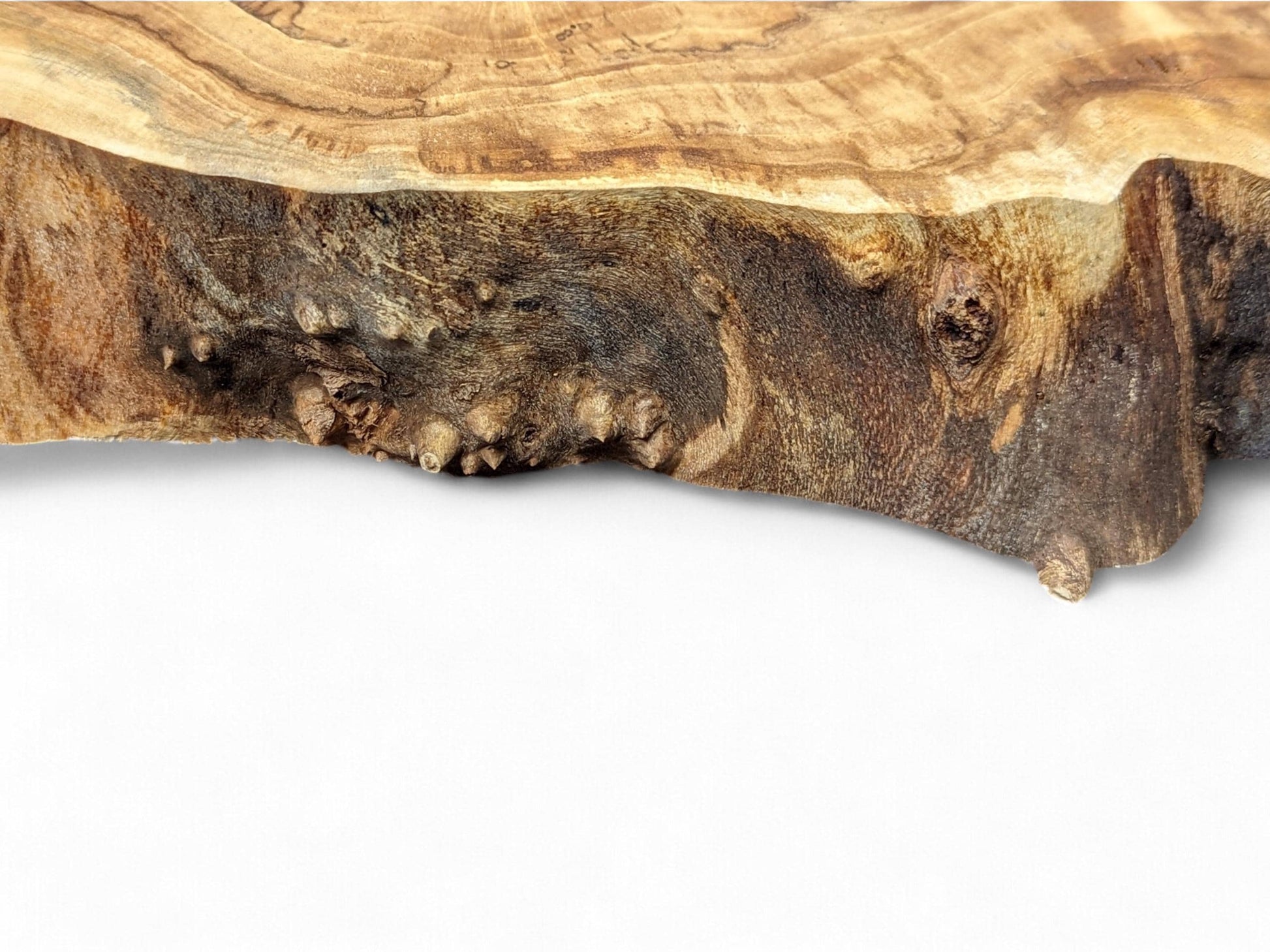 Wood slice with light brown wavy grain, and a dark, textured live edge covered in small knots.