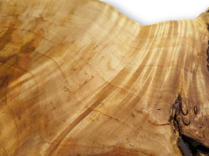 Close-up of a light golden-brown live edge wood slice with prominent wavy grain and dark crevices.