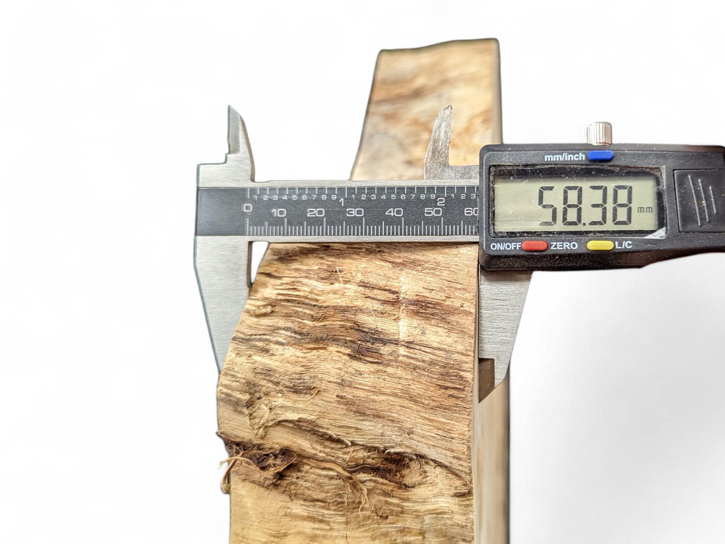 Caliper measuring the light brown, irregularly textured wood slice, displaying a thickness of 58.38 mm.