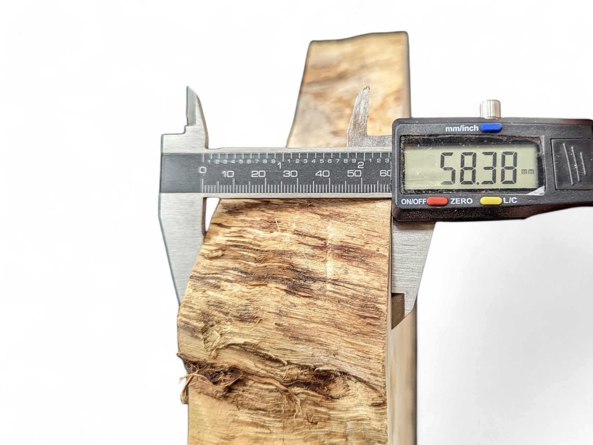 Caliper measuring the light brown, irregularly textured wood slice, displaying a thickness of 58.38 mm.