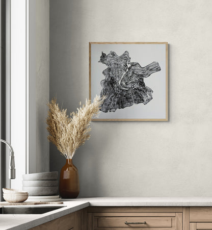 A framed black and cream monoprint of a tree root slice hangs above a kitchen counter.