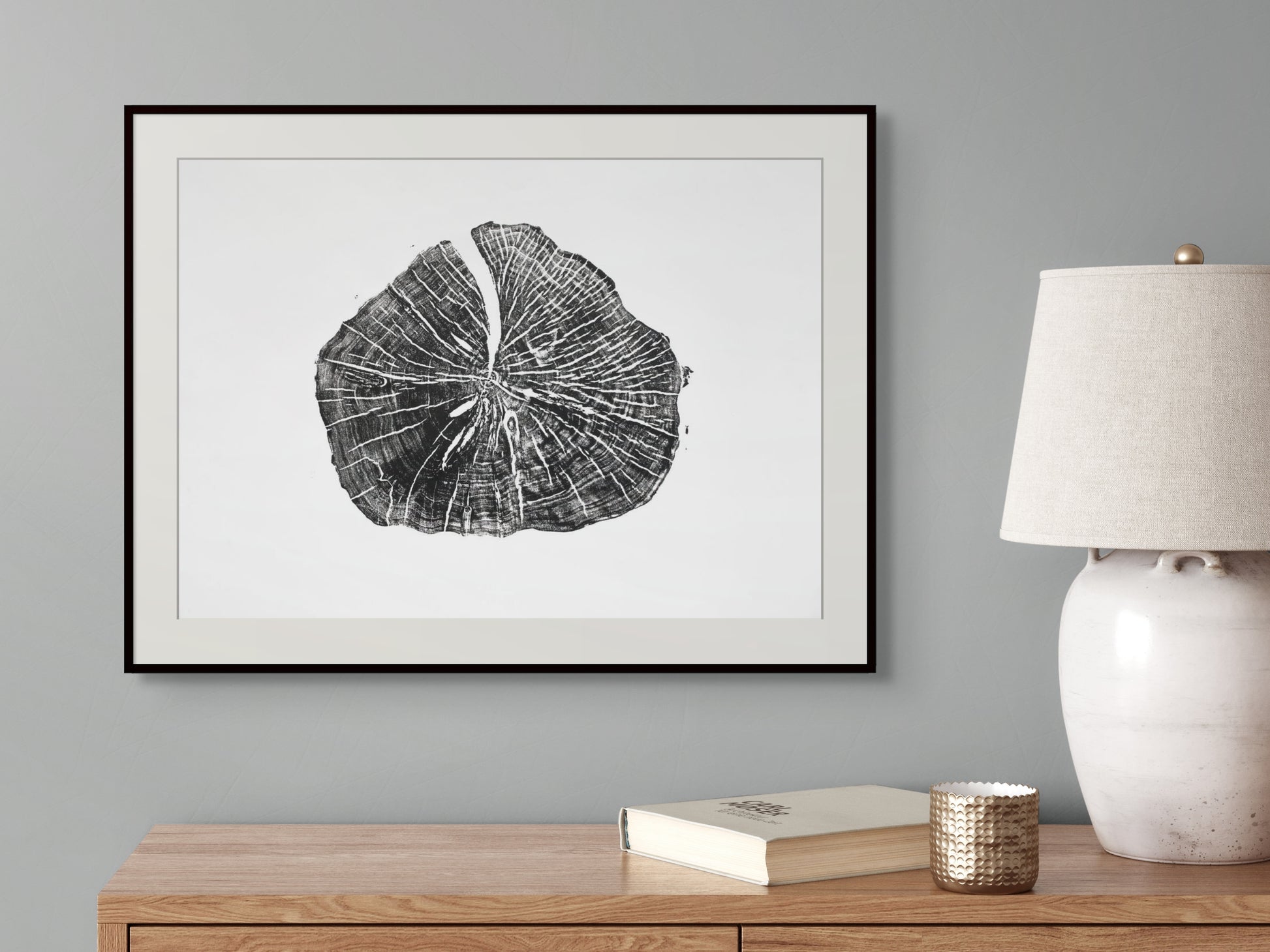 A framed black and white tree ring print hangs on a grey wall above a wooden table.
