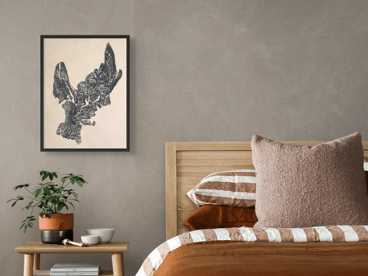 A framed dark woodcut monoprint of a tree root impression hangs on a greige wall above a bed.