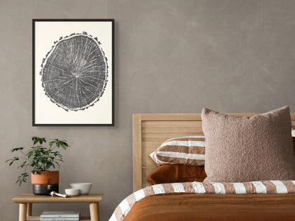 A framed black and white tree ring print with detailed concentric circles on a grey wall.